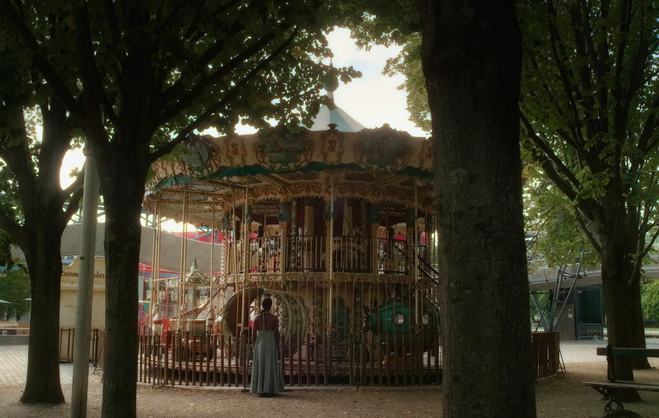 Eine Frau steht vor einem historischen Karusell unter Bäumen